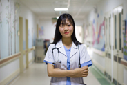 A photo of a asian female doctor standing in the hallway of a hospital.