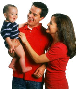 Photograph of a father-figure holding a smiling baby and a mother-figure.